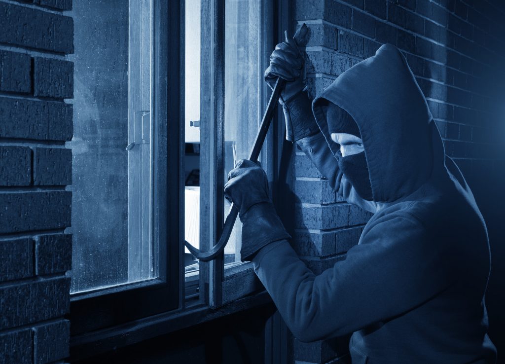 Burglar uses the crowbar to break into a house at night. Prevent home break-ins.