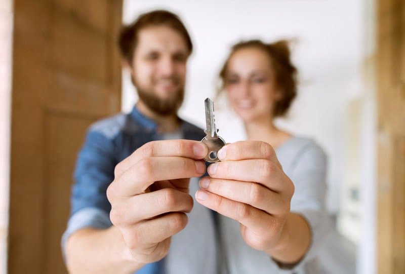 Young married couple moving into a new house, holding a key together.
